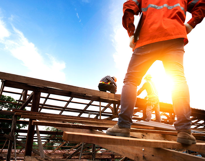 engineer in a hard hat holding a laptop and looking at a team of wood roofers